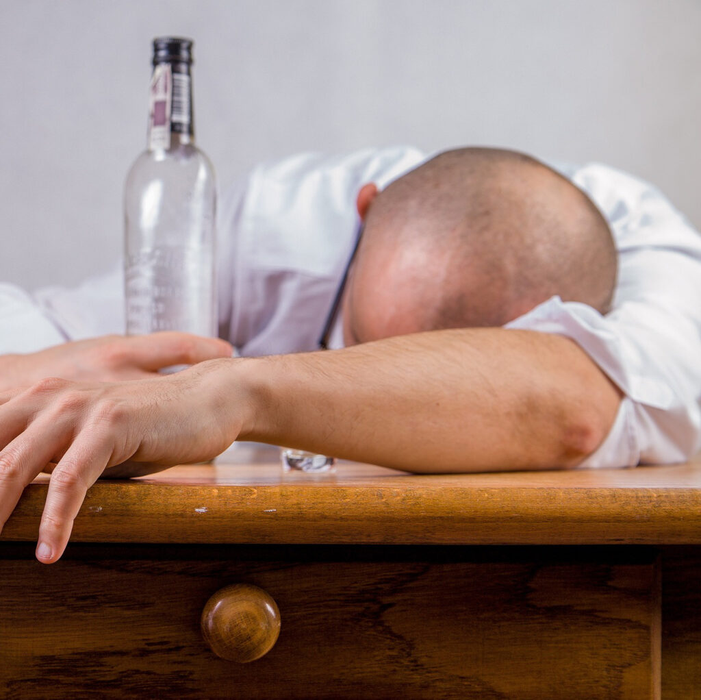 Drunk man holding a bottle of alcohol while sleeping on a table