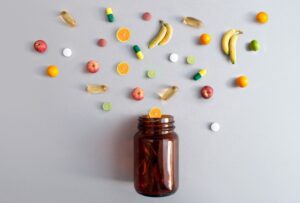 Vitamin pills and capsules alongside apples, bananas, lime and oranges coming out of a medicine jar, nutrition concept.
