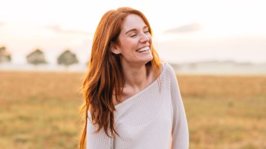 A woman smiling in a grass field.