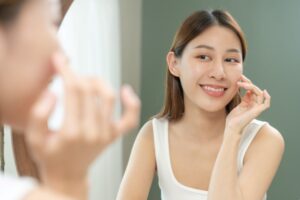 Young woman looking on reflection in mirror, hand touching face during skin care routine.