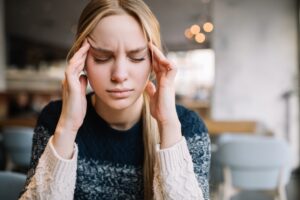 A woman holding her head in pain while she struggles with a migraine.