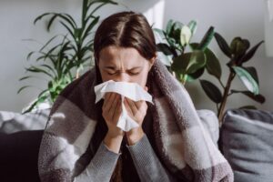 A woman blowing her nose and struggling with the flu during flu season.