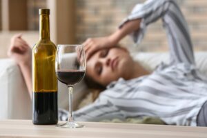 A woman waking up hungover and looking at the bottle of wine and glass from the night before.